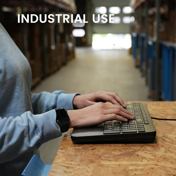 Hands typing on a slim keyboard at wooden desk in industrial warehouse setting, with 'INDUSTRIAL USE' text overlay.